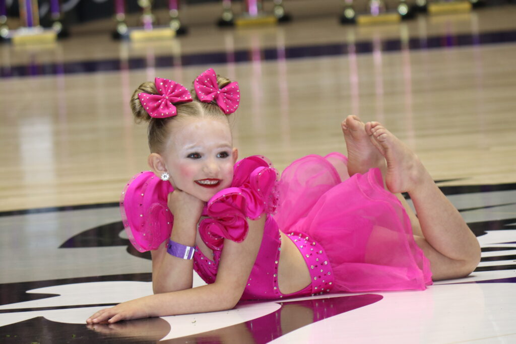 Young girl in a bright pink dance costume posing with a smile.