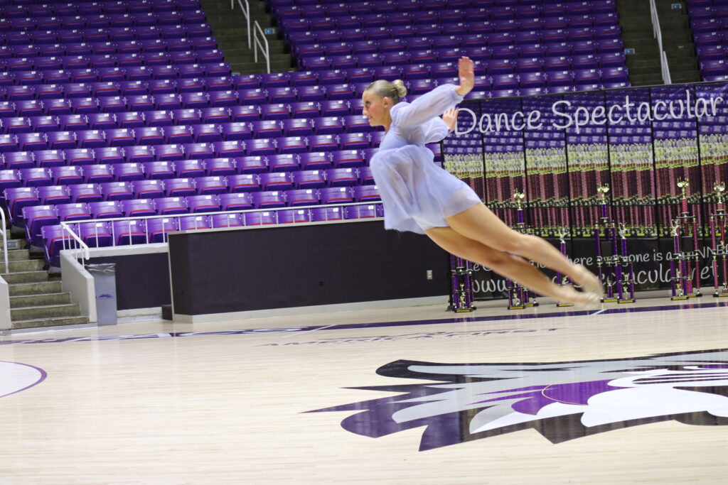A dancer leaps gracefully mid-air in a purple-themed arena.