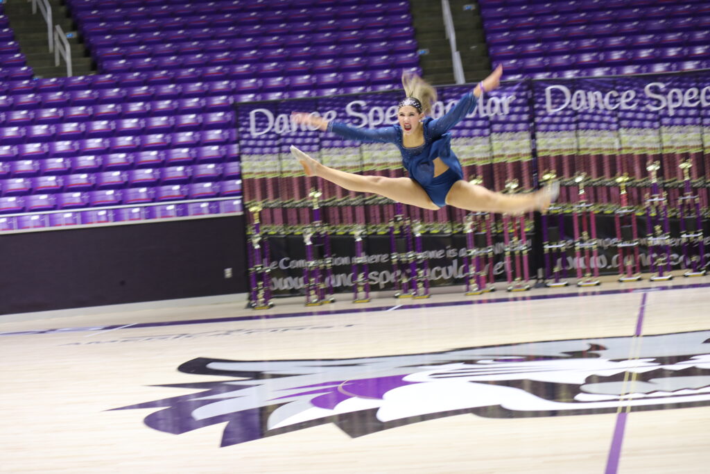 A gymnast performing a leap on a gym floor.